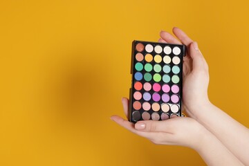 Woman with bright eyeshadow palette on yellow background, closeup. Space for text