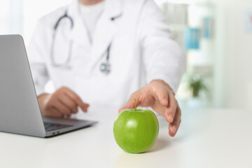 Nutritionist taking green apple at table in clinic, closeup