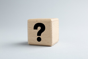 Wooden cube with black question mark on light grey background, closeup