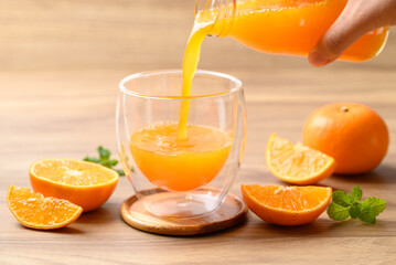 Orange juice pouring into glass with orange fruit on wooden background, Healthy drink