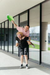 Two cheerful young men celebrate outdoors with a playful piggyback ride and joyful laughter,...