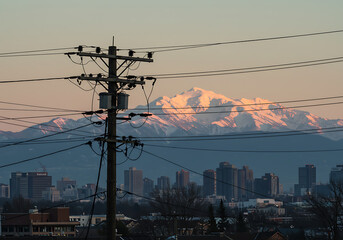 The sunset casts a warm glow over snowy mountains in the background of a cityscape scene.