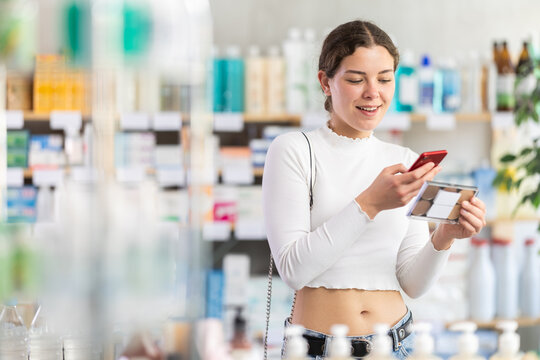 Young woman scans mobile barcode of makeup powder palette. Buying and paying for makeup products at the pharmacy