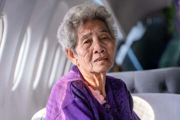 Senior Asian gray haired woman looking at camera. Portrait of an elderly woman sitting in a window seat of an airplane in cafe.