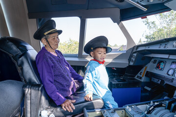 Grandmother and grandson at controls of airplane sitting in cockpit wearing a pilot hat and sitting in an airplane cockpit, smiling confidently, portraying dreams of aviation and  future of flight.