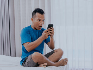 Wow face of Asian man surprised while look at the mobile phone in his apartment.