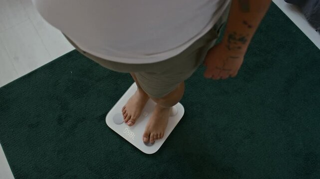 High angle shot of unrecognizable tattooed female dieters stepping on digital scale to check weight loss progress