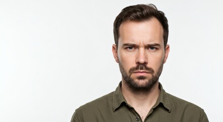 Obraz premium A man with a beard and an olive green shirt looking directly at the camera with a serious expression
