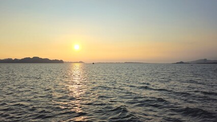 A serene sunset over the waters of Ha Long Bay, Vietnam, with the sun reflecting on the gentle waves and silhouetted islands in the distance.