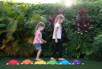 Two happy girls running and playing outside on artificial grass with colorful turtle stepping...