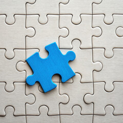 Fototapeta premium Blue puzzle piece is placed on top of nearly completed beige puzzle, symbolizing final step or missing part in project or idea, evoking sense of completion and focus