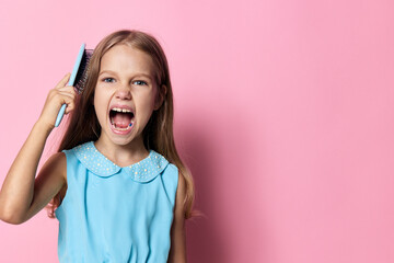 Little girl with curly hair smiling and holding a comb above her head, gazing upwards at the camera