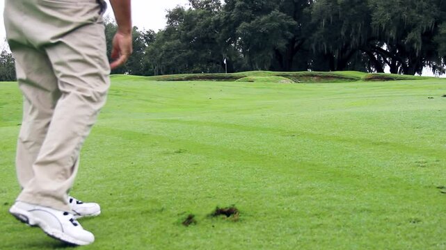 Golfer makes divot with swing to hit ball by flag on the green