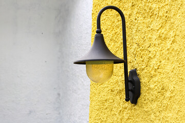 Black vintage wall lamp mounted on textured yellow wall in daylight.