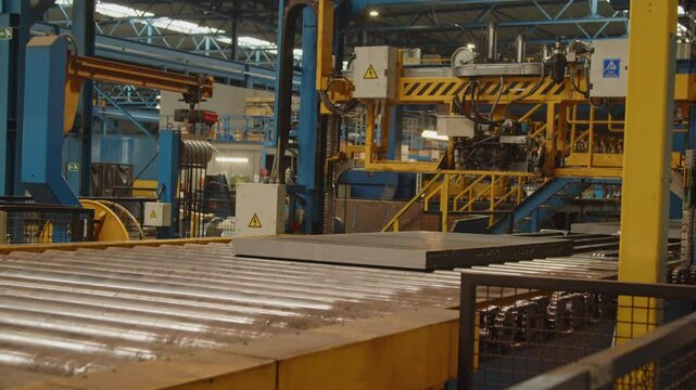 A stack of steel plates are bound together by an automated arm and rolls over a roller bench