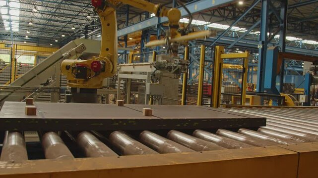 An automated arm places dividing wood blocks on a stack of steel plates on a roller bench