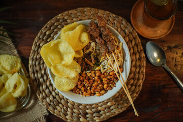 Delicious Indonesian chicken porridge (bubur ayam) served with crispy crackers, shredded chicken, skewered liver, and savory roasted peanuts. Perfect traditional breakfast or street food delight.
