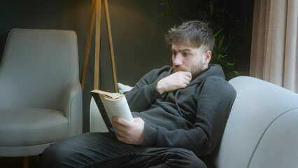 Young man reading a book and relaxing in a cozy living room with warm ambient lighting