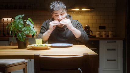 Young man enjoying late night snack at kitchen table giving thumbs up