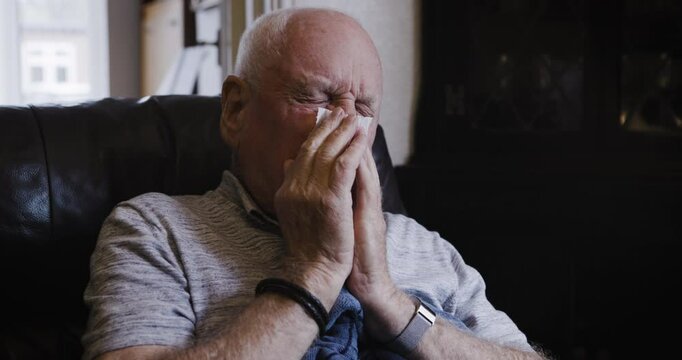 Sick, cough and sneezing old man blowing nose, tissue and illness in living room. Throat pain, thyroid cancer and senior sneeze, flu and cold, covid 19 and corona virus, health or acid reflux problem