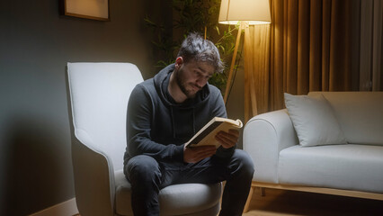 Young Man Relaxing at Home Reading a Book in Cozy Evening Lighting