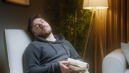 Young Man Peacefully Asleep in Armchair After Reading a Book at Night