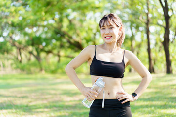 Fototapeta premium Asian woman take a break and drinks water from bottle after finished running.