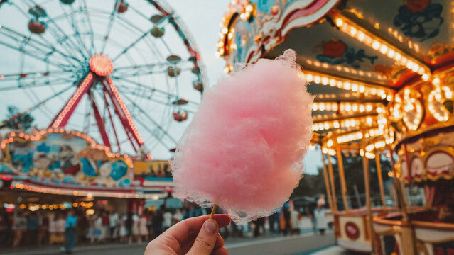 Cotton Candy Carnival: A whimsical scene unfolds, showcasing a vibrant pink cotton candy held in hand against the backdrop of a colorful carnival, evoking childhood nostalgia and pure joy.