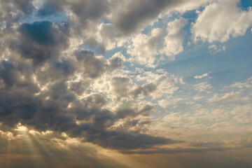 Sunlight streams through a moody sky filled with dark and light clouds, creating a dramatic and...