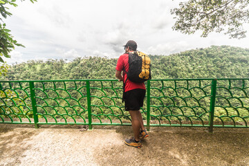 Adult man wearing sportswear and backpack observing a landscape with a mountain view surrounded by tropical forest on a cloudy day in the Costa Rican jungle