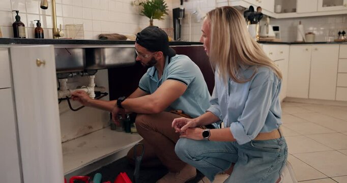 Plumber, repair and handyman with woman in kitchen for maintenance, installation service or renovation. Discussion, inspection and man talking to client with pipe to explain leak or sink problem