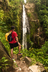 Vertical shot of an adult male hiker posing in front of a landscape with a waterfall of pure water in the middle of the mountain surrounded by tropical forest and Costa Rican jungle