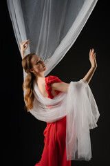 Woman in a red dress expressing emotion while posing elegantly in a studio, draped in sheer fabric...