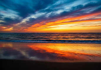 Fototapeta premium spectacular sunset over the ocean reflecting vibrant colors on the beach