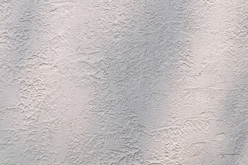 A close-up texture of a rough, light gray plaster wall with subtle patterns, showcasing a raw and natural surface with a slightly uneven finish