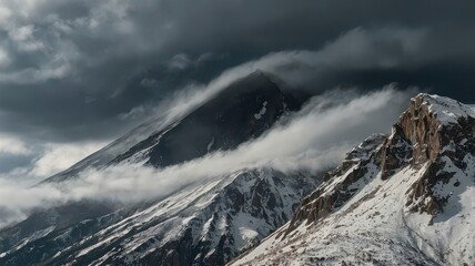 A view of snow capped mountains partially covered by clouds under a dark and stormy sky in the wilderness
