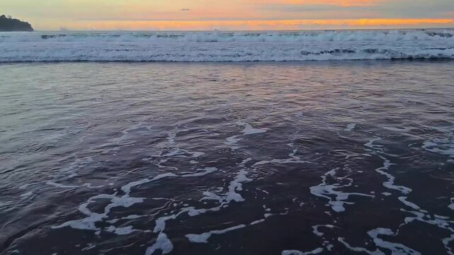 Crushing wave in sunset. Tide on the beach.From a distance seen the rolling and breaking of the sea waves,foam shaped wave current flows to the beach.
