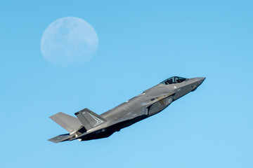 F35 flying past moon on a clear blue day