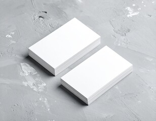 Two pristine, blank business cards lie side by side on a smooth grey background, showcasing their clean white surfaces and subtle shadows.