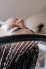 Close-up of a woman receiving a head massage during a Japanese head spa treatment with water flowing from a special hair washing tool, focusing on the scalp relaxation and beauty therapy