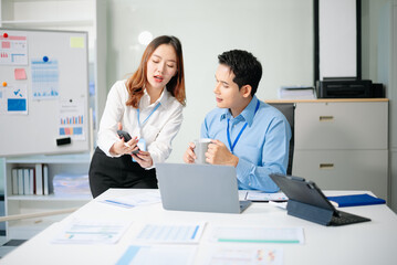 Fototapeta premium Two young Asian professionals engaged in teamwork and business discussions in modern office embodying corporate