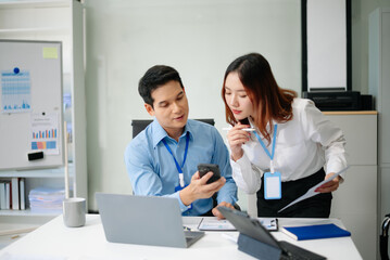 Obraz premium Two young Asian professionals engaged in teamwork and business discussions in modern office embodying corporate