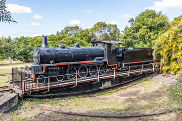Fototapeta premium A retired old steam locomotive and coal truck on a turntable for turning trains around at the end of the line against a background of trees and sky at Imbil in Queensland, Australia.
