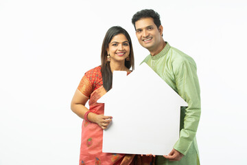 Indian happy traditional couple holding a home shape paper craft on white background on the occasion of Indian festivals.  and Home loan theme and advertisement promotions