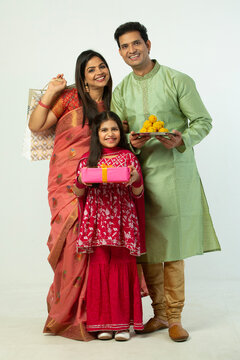 Indian happy traditional family holding shopping bags, gift boxes and sweets laddu on studio background in Diwali festival 