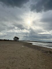 the spring sun breaks through the grey clouds over the water and deserted beach
