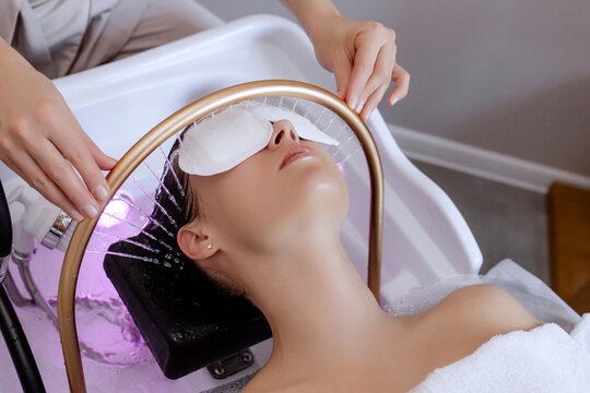 Close-up of a woman receiving a Japanese head spa treatment, relaxing with eye pads and water droplets from a special tool for scalp massage, part of a beauty therapy session