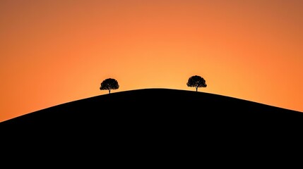 Two Silhouetted Trees Standing atop a Blackened Hill Under a Warm Sunset