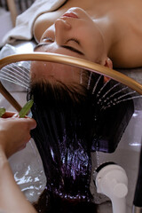 Close-up of a woman receiving a relaxing Japanese head spa treatment, with green massage sticks applied to her scalp, while water gently flows from a special tool during the session in a beauty salon