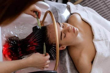 Foto auf Acrylglas Massagesalon Close-up of a woman receiving a relaxing Japanese head spa treatment, with green massage sticks applied to her scalp, while water gently flows from a special tool during the session in a beauty salon  © MarijaBazarova